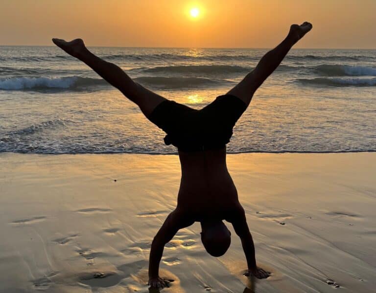 Person macht einen Handstand am Strand bei Sonnenuntergang mit Blick auf das Meer