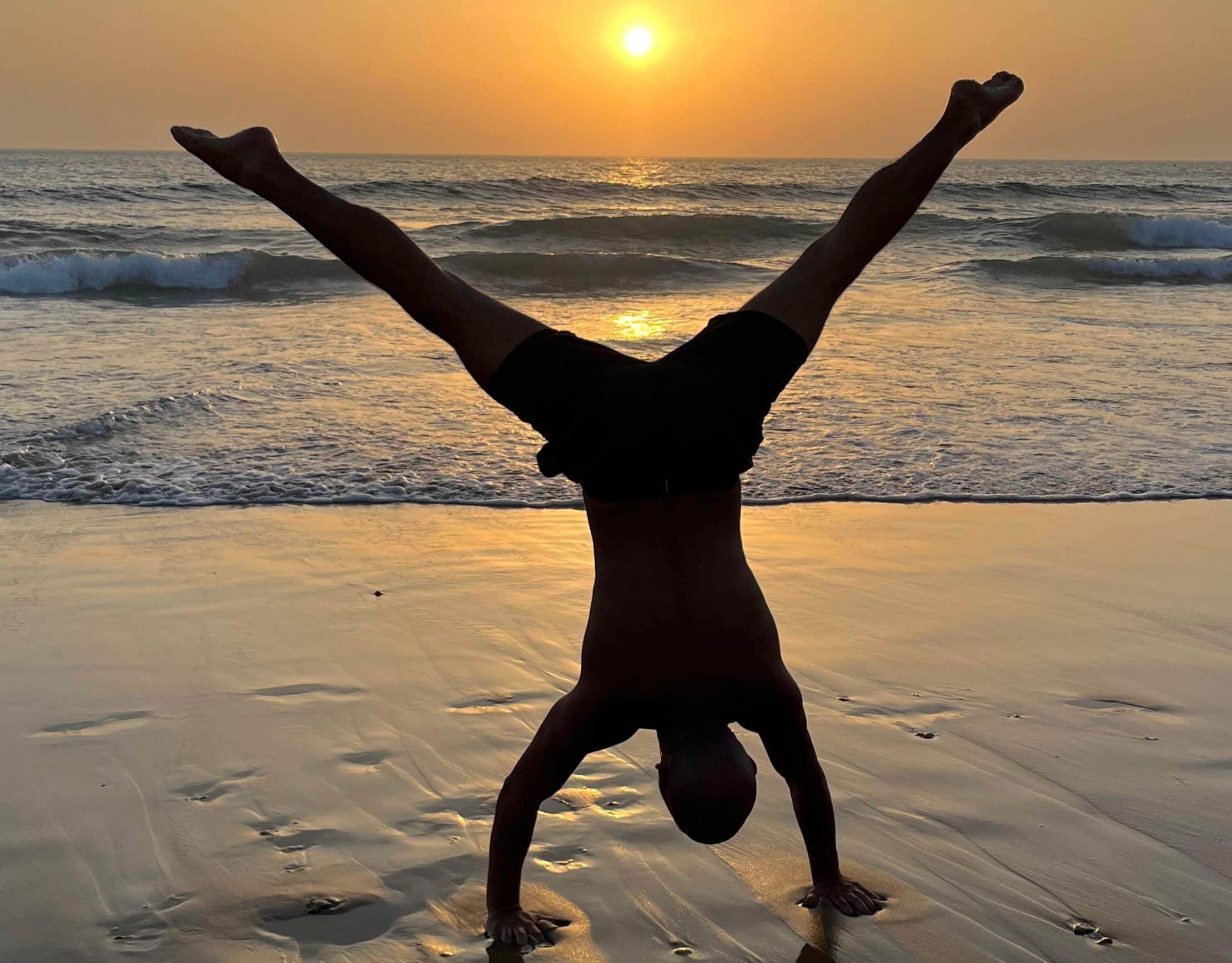 Person macht einen Handstand am Strand bei Sonnenuntergang mit Blick auf das Meer