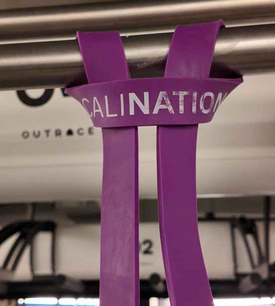 Lila Widerstandsband an einer Klimmzugstange befestigt, ideal als Unterstützung beim Klimmzüge lernen im Fitnessstudio.